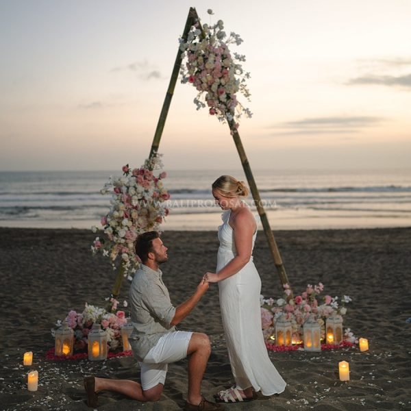 Couple under a beach cave with a red rose heart and a Will You Marry Me neon sign